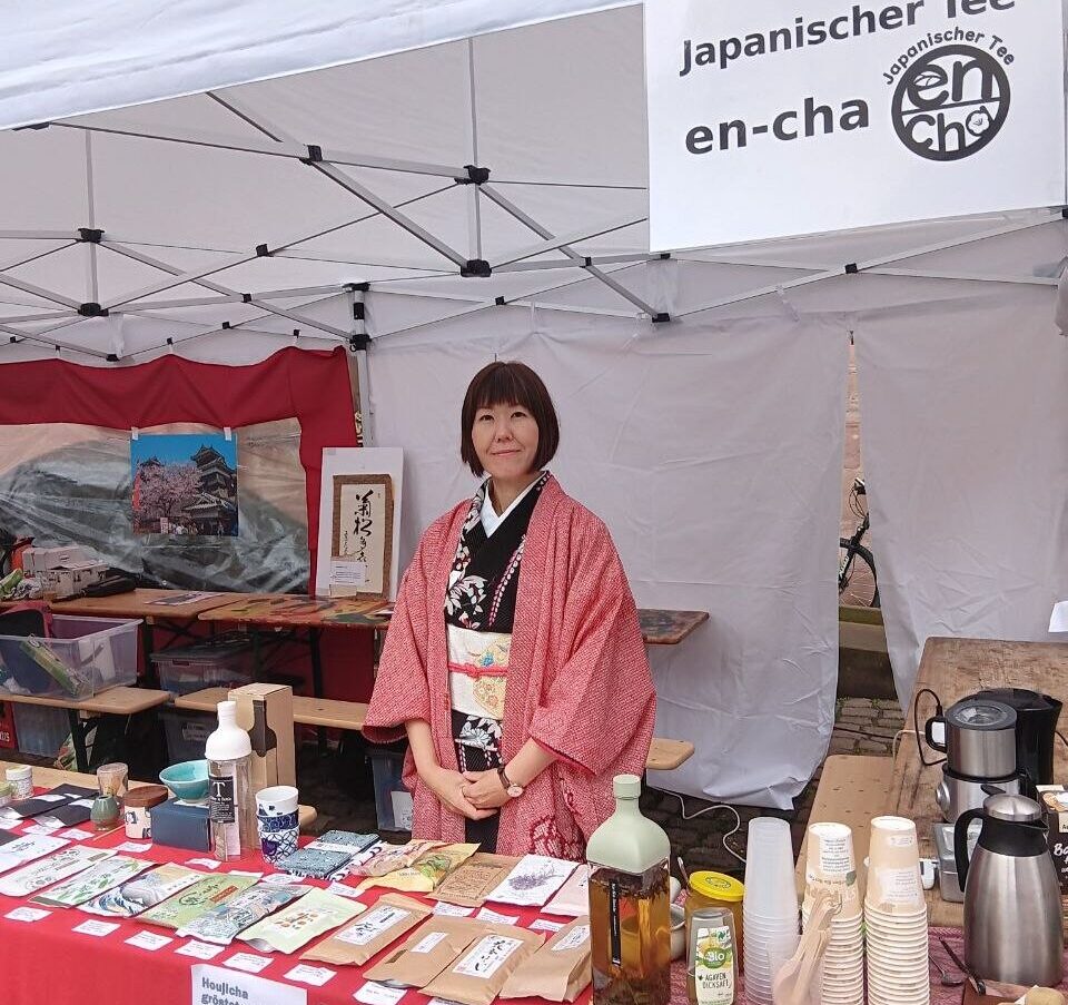 Zu sehen ist eine japanische Dame hinter einem Stand, an dem loose Tees zu erwerben sind